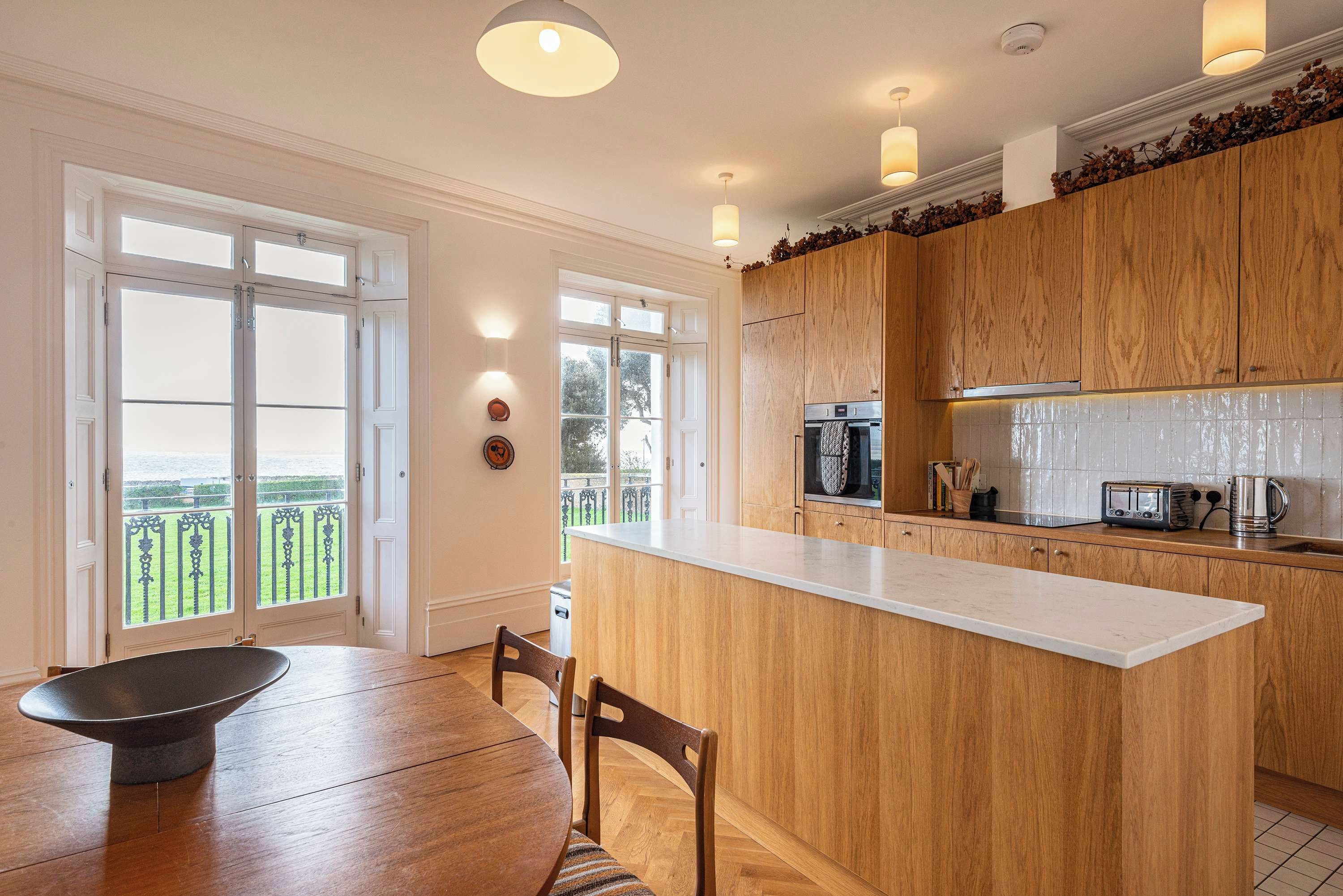 A modern kitchen with wooden cabinets, a central island, and a dining area with a table and chairs.