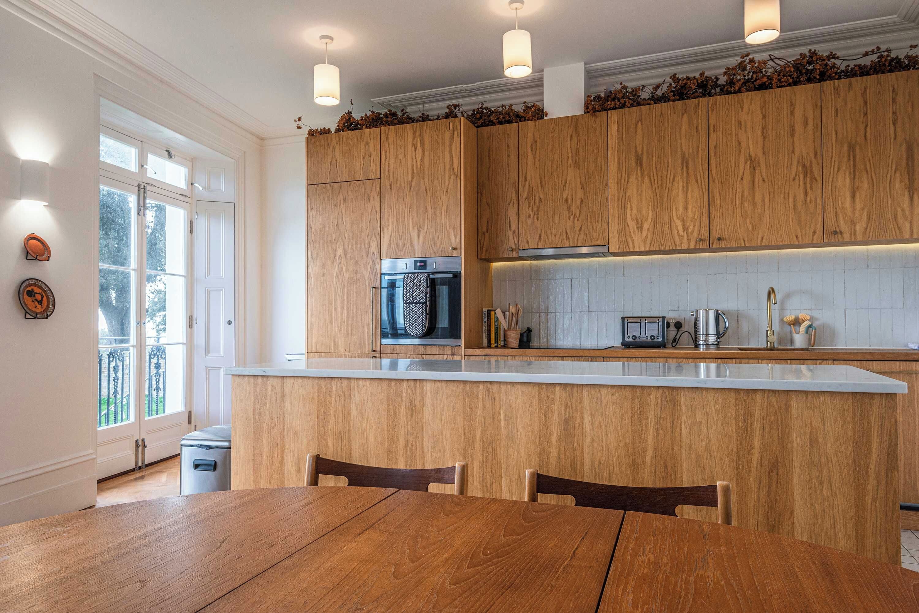 Une cuisine moderne avec des meubles en bois, un îlot central et un coin repas comprenant une table et des chaises en bois.