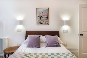 A bedroom with a bed, two wall-mounted lamps, a radiator, and a poster on the wall. - Royal Channel Retreat | Peaceful Sea Views (Ramsgate)