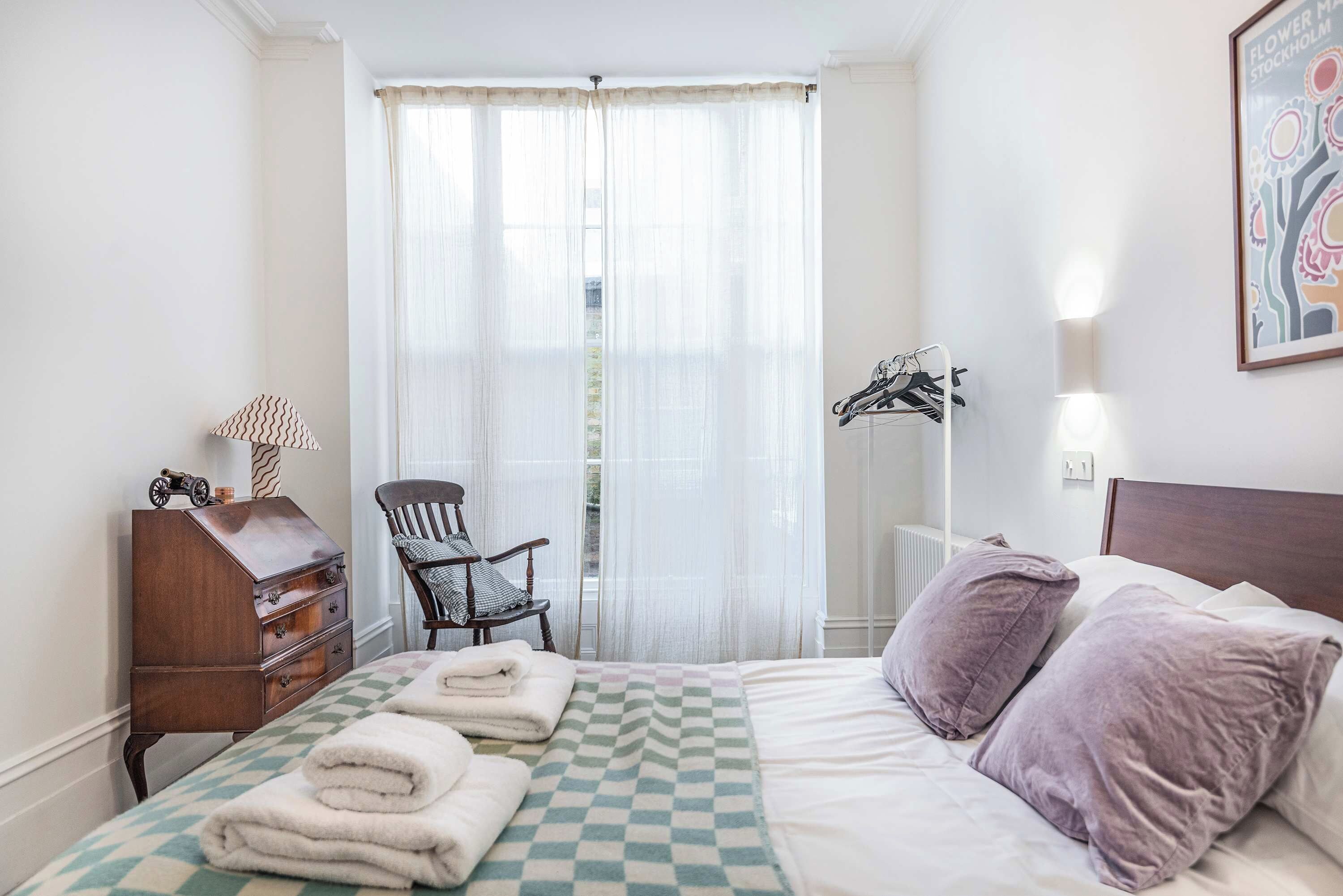 A hotel room with a bed, a chair, a dresser, and a coat rack.