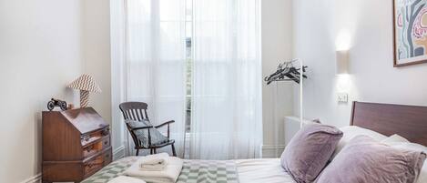 A hotel room with a bed, a chair, a dresser, and a coat rack.