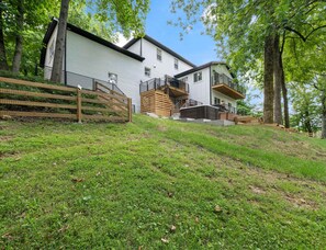 Ein zweistöckiges Gebäude mit weißer Fassade, einer Holzterrasse und einer Treppe, die zu einem Balkon führt.