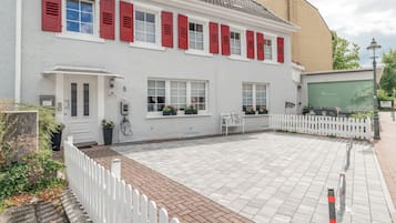 Ein weißes Gebäude mit roten Fensterläden, einem gepflasterten Innenhof und einem weißen Ziergartenzaun.