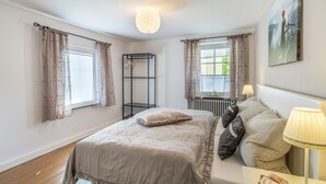 Un dormitorio con cama, mesita de noche, lámpara y ventana con cortinas.