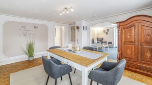 Un comedor con una mesa y sillas de madera, una planta en maceta y una pared con un mensaje decorativo.