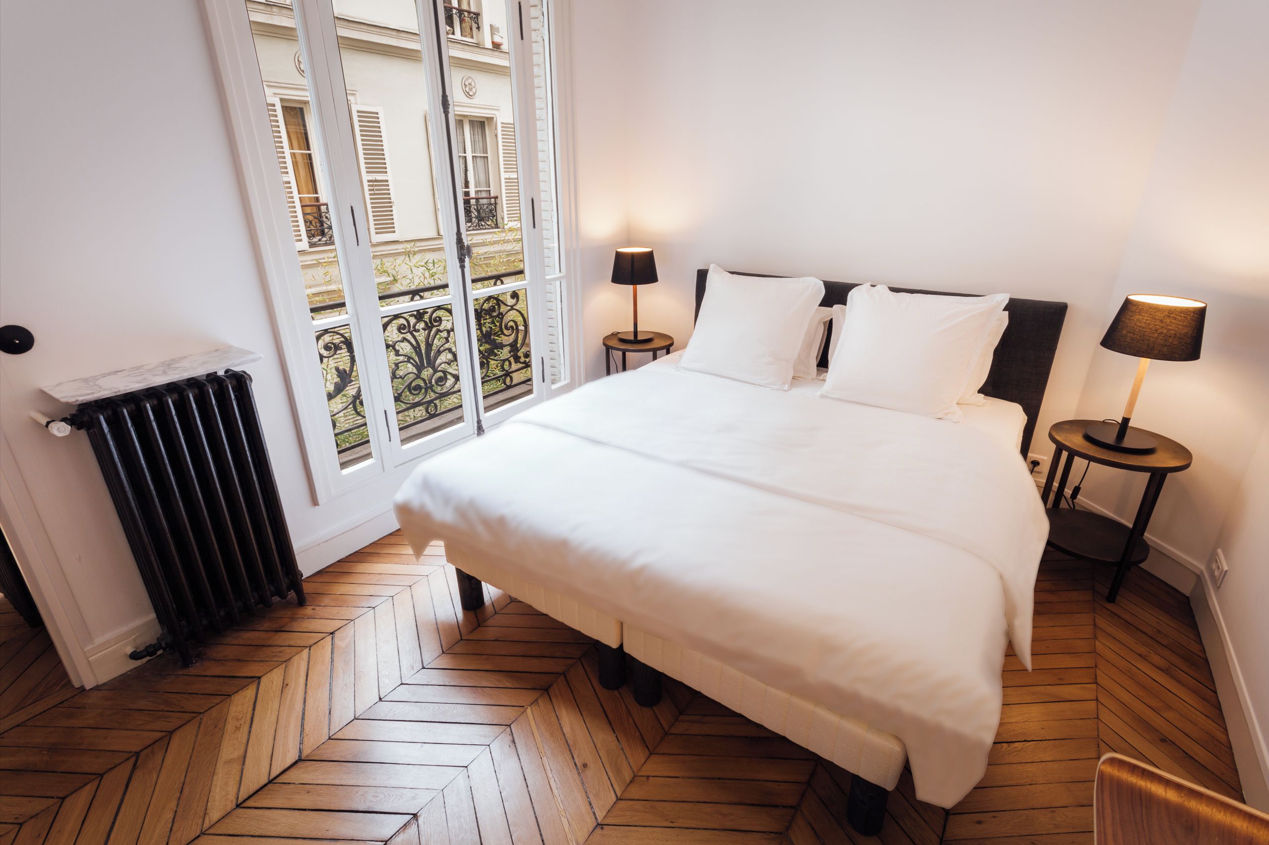 Een hotelkamer met een groot bed, twee nachtkastjes, een radiator en uitzicht op buiten.
