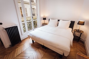 Une chambre d’hôtel avec un grand lit, deux tables de chevet, un radiateur et une vue sur l’extérieur.