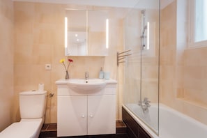Un baño con inodoro, lavabo, espejo y ducha con mampara de vidrio.