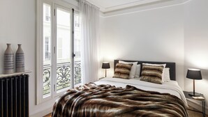 A bedroom with a bed, two bedside lamps, a fur throw, and a view of the outside through a window with curtains. - Luxury 1BR steps away from Champs Elysees (Paris)