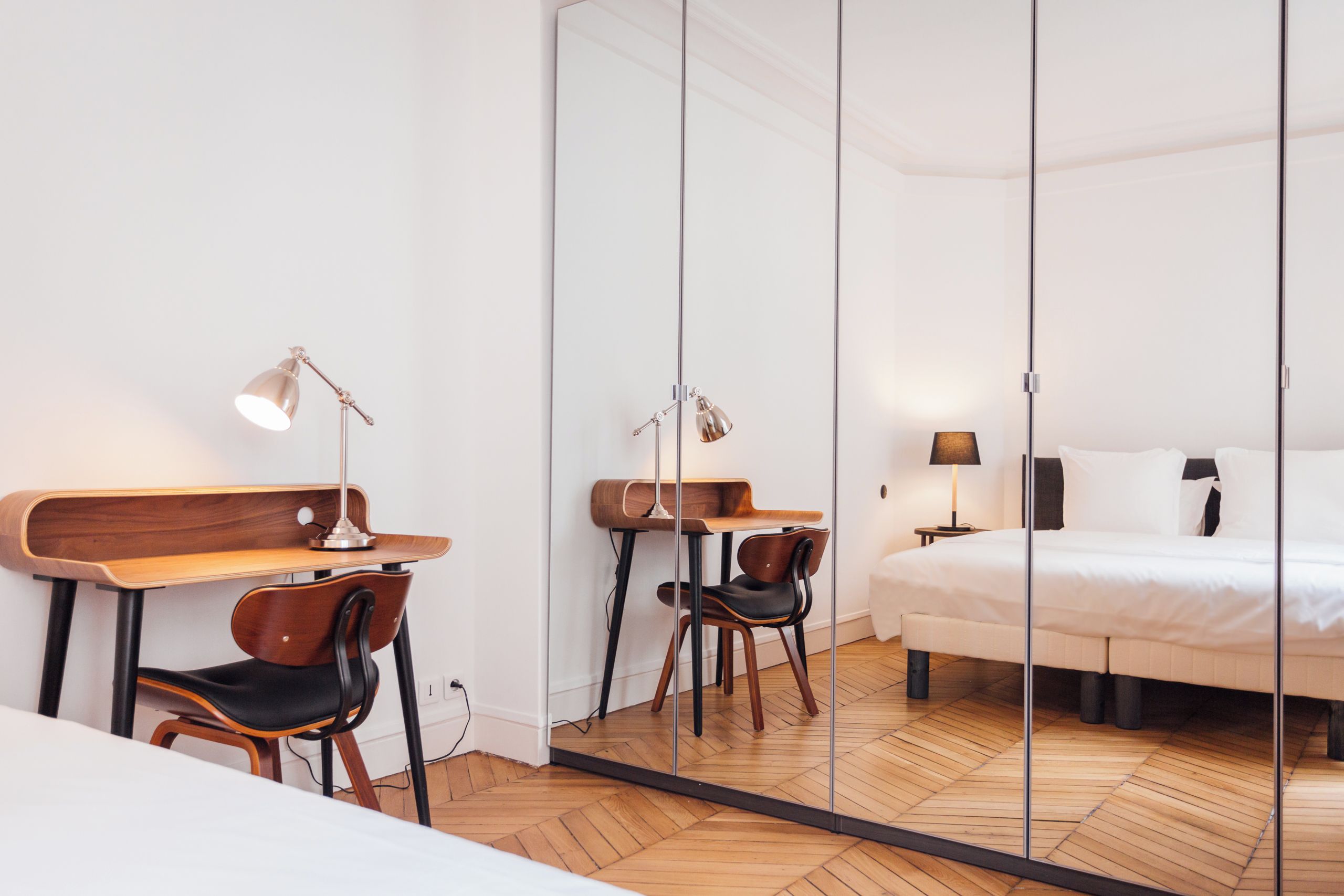 Een hotelkamer met een houten bureau, een stoel, een bed en een spiegel.