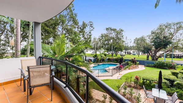 Un balcon avec vue sur une piscine, entouré de verdure et donnant sur un parc.