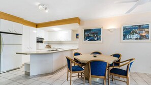 Une cuisine moderne avec des meubles blancs, un îlot central et un coin repas doté de chaises bleues.