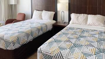 Quarto de hotel com duas camas, cada uma com colcha estampada, mesa de cabeceira, luminária e uma cadeira.