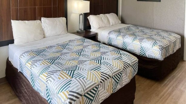 A hotel room with two beds, each with a patterned bedspread, a bedside lamp, and a framed picture on the wall. - 2 Full Beds | Smoking (Opelika AL)