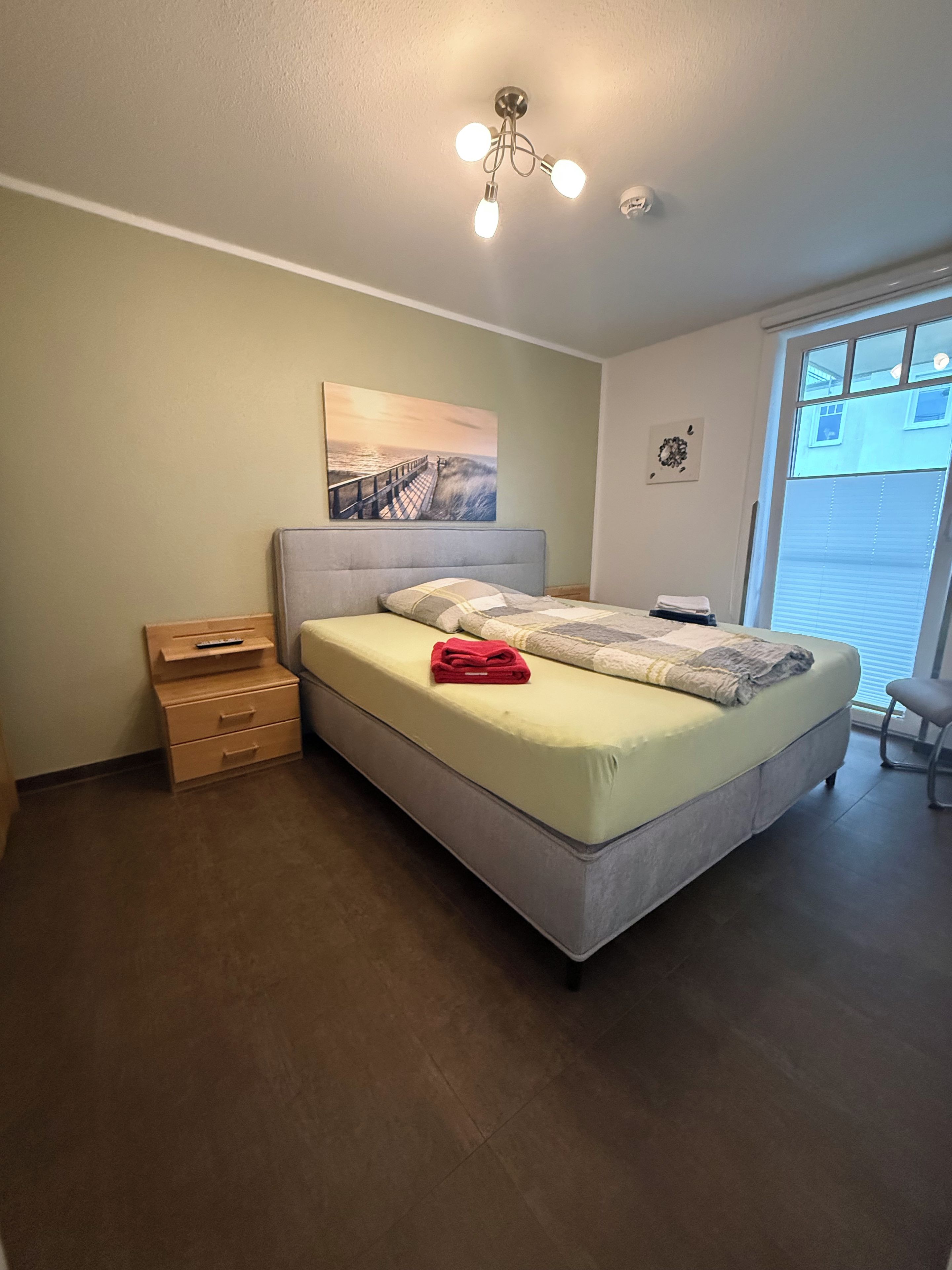 A bedroom with a bed, a nightstand, a dresser, a painting, and a window.