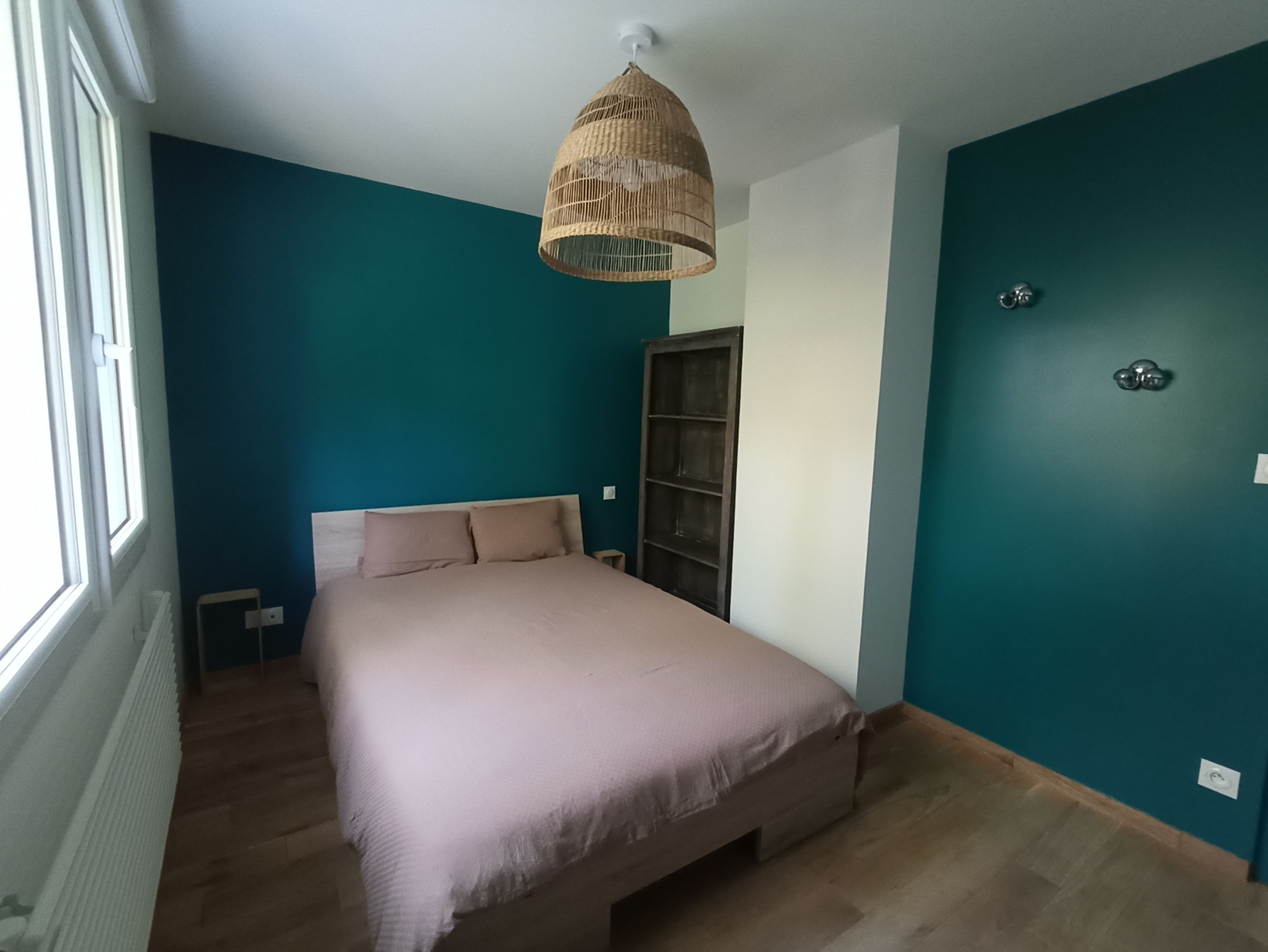 A bedroom with a bed, a window, a wall-mounted shelf, and a ceiling light fixture.