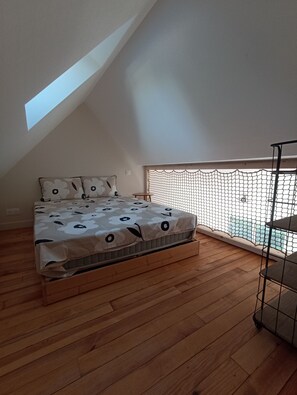 Ein Schlafzimmer mit schrägen Wänden, einem Bett mit blumigem Überwurf, Holzboden und einem Balkon mit Metallgeländer.