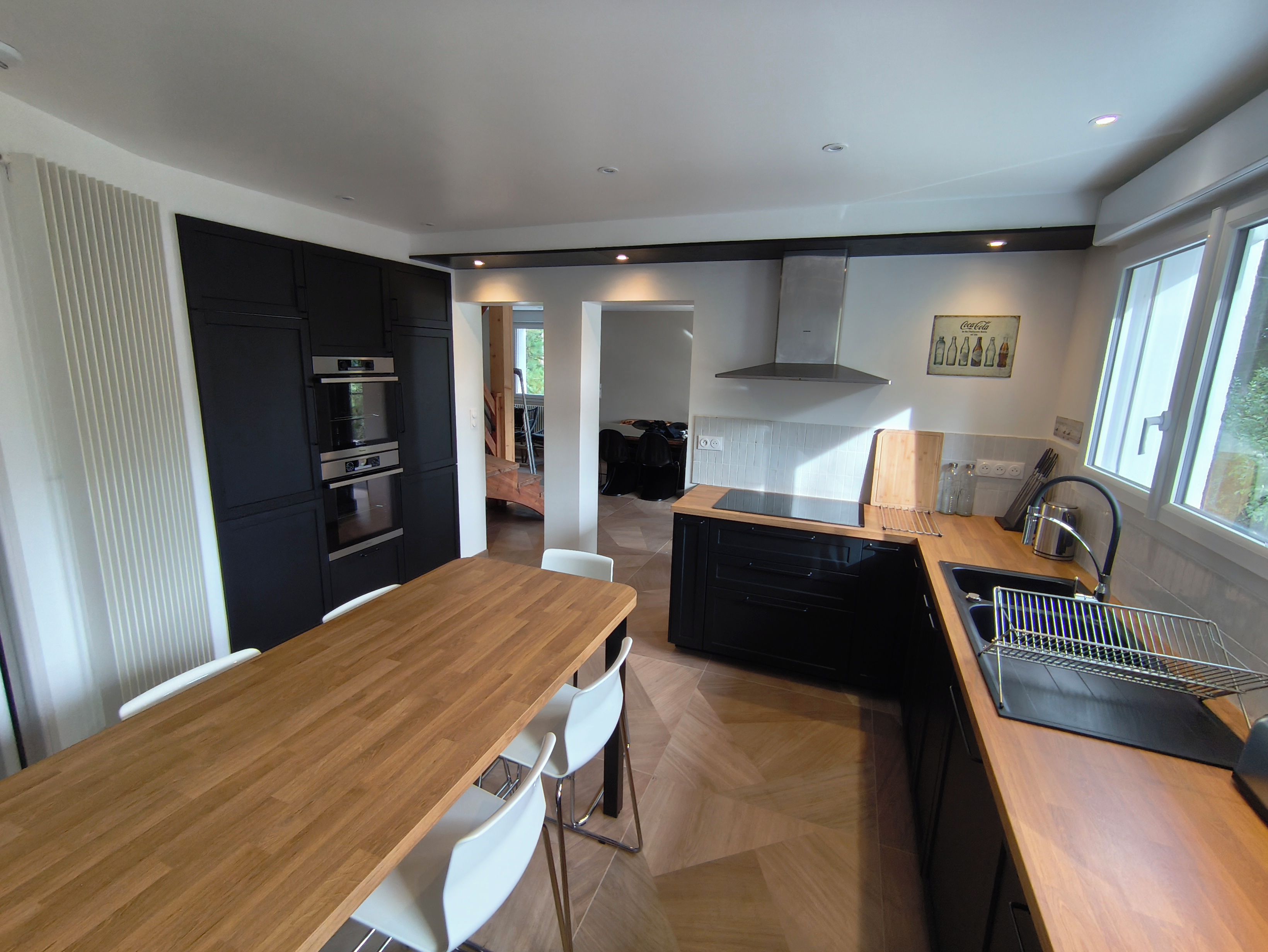 A modern kitchen with a wooden dining table, white chairs, and built-in appliances.