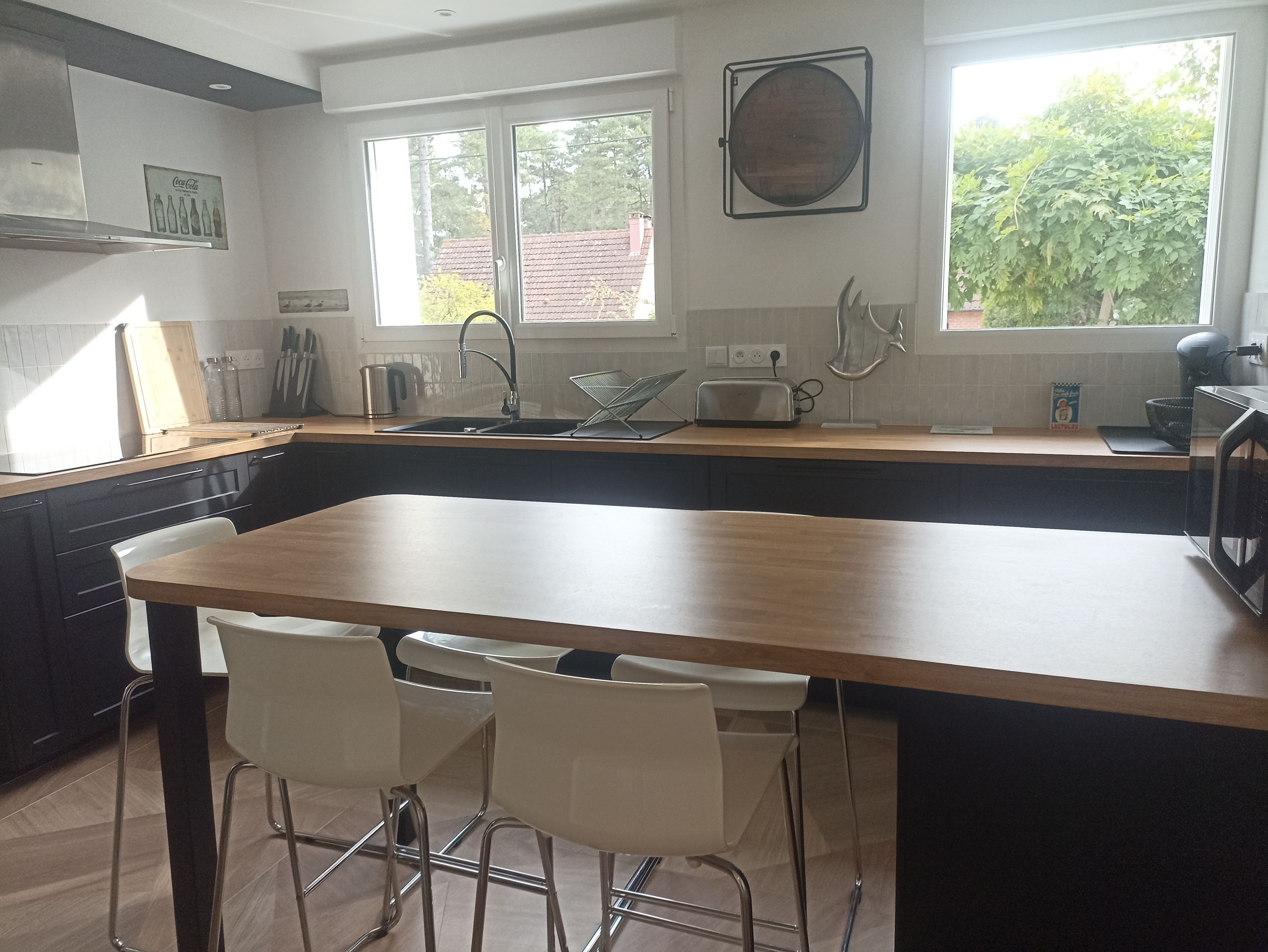 A modern kitchen with a central island, bar stools, and a window providing a view of the outdoors.