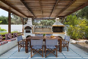 Une terrasse extérieure avec une table et des chaises en bois, un barbecue intégré et un coin salon agrémenté de coussins.