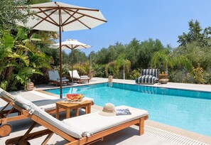 Ein Poolbereich mit Liegestühlen, Sonnenschirmen und einem Tisch mit Obst und einer Zeitschrift.