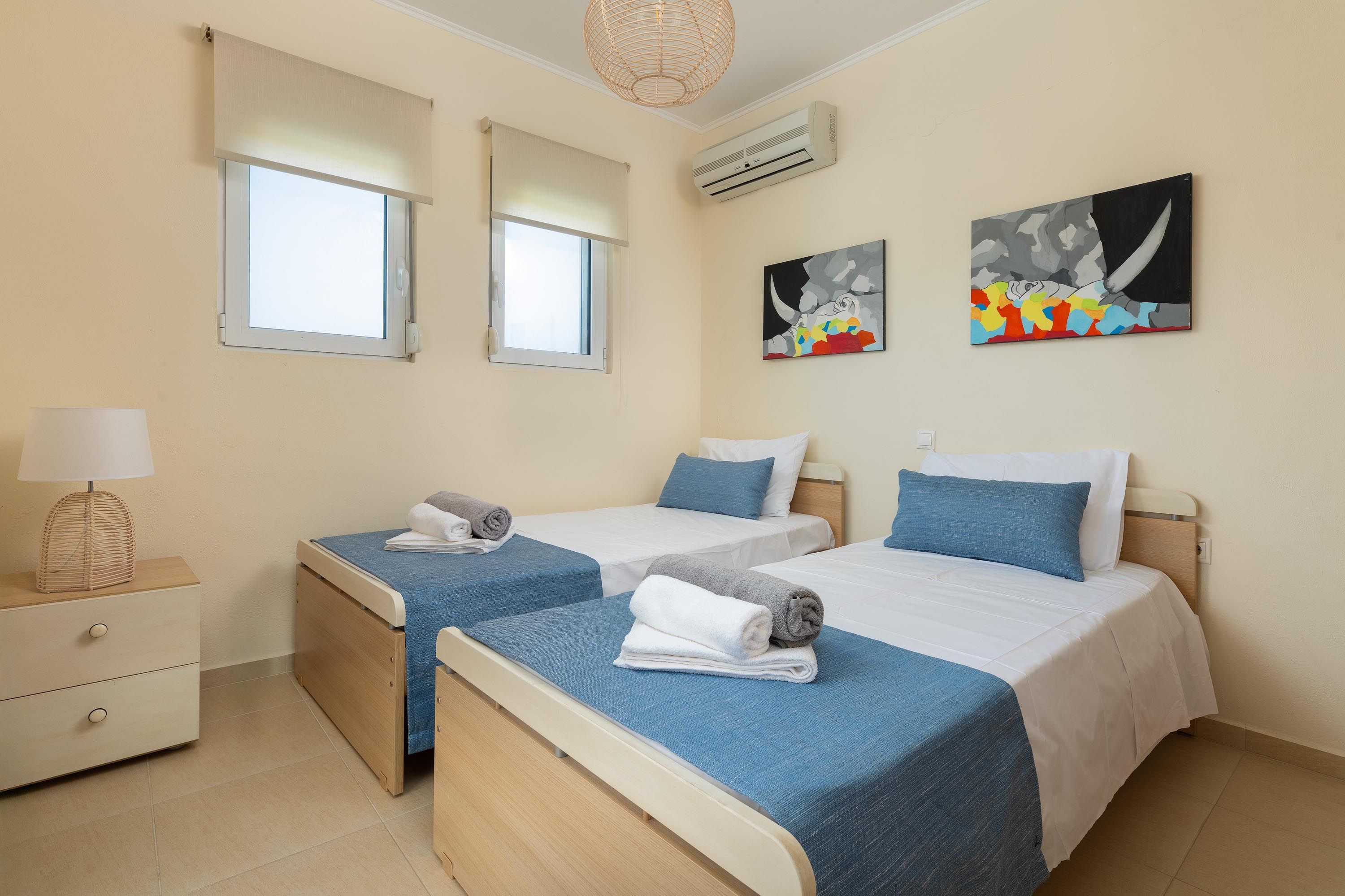 A hotel room with two beds, a bedside table with a lamp, and artwork on the walls.