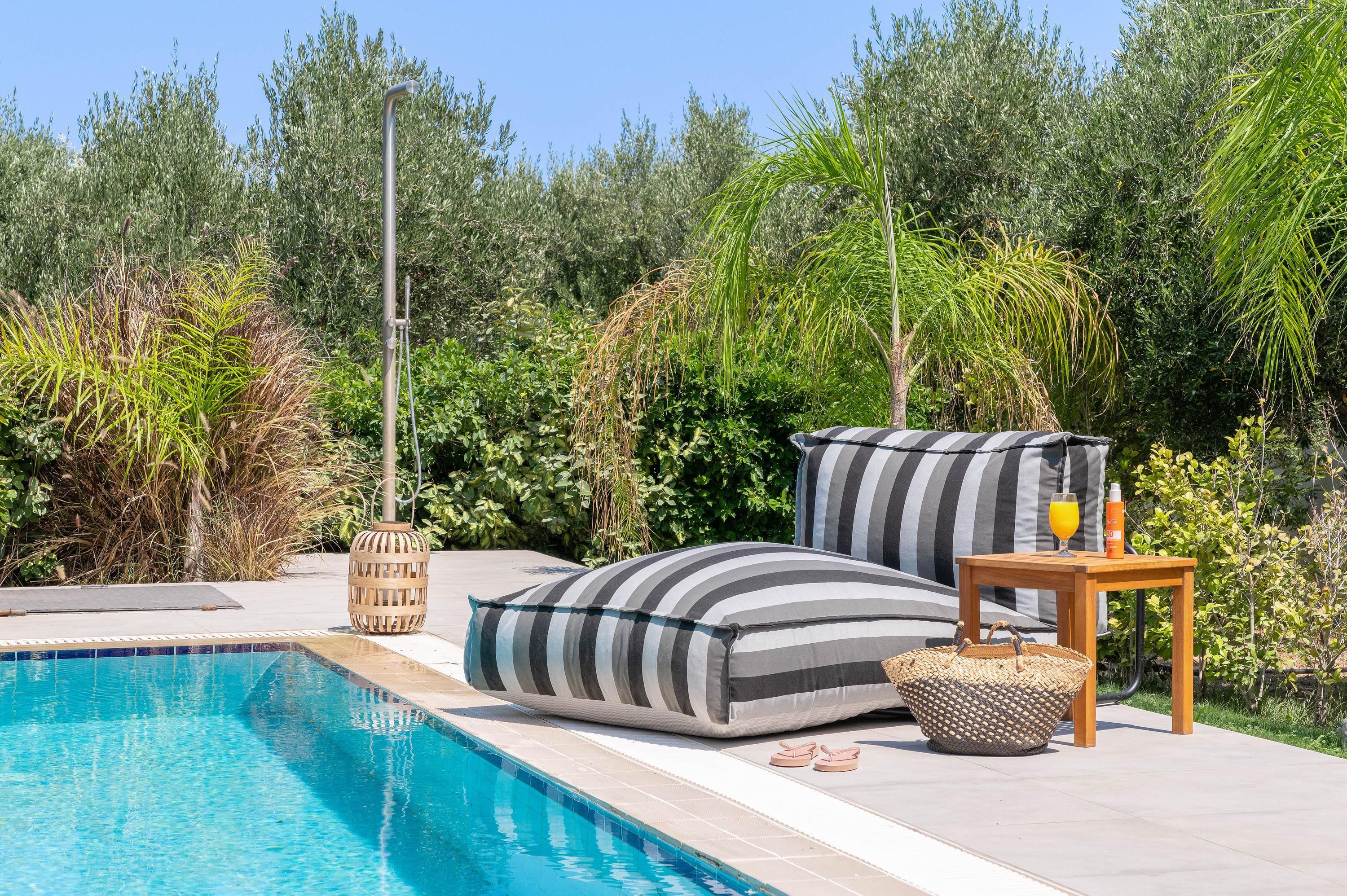 Zona junto a la piscina con piscina, sillas de descanso, una mesa con una bebida y una botella de protector solar.
