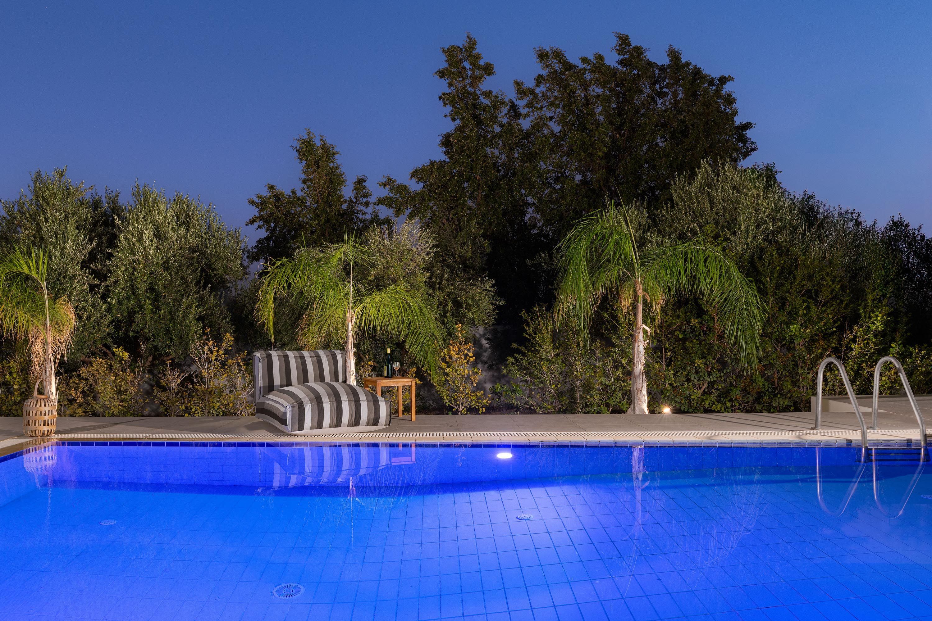 A swimming pool with a tiled deck, a lounge chair, and a small table with a bottle and glass.