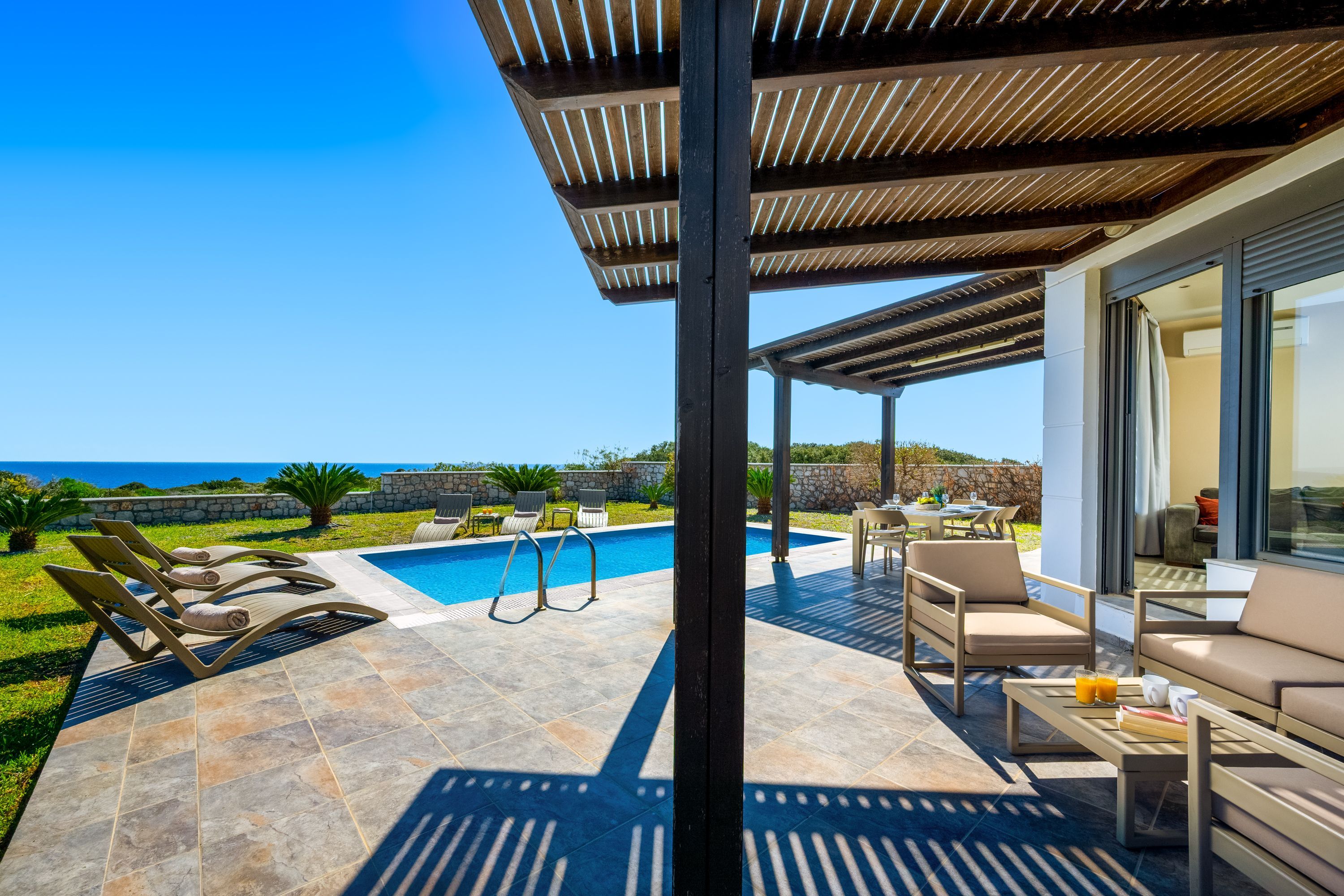 Ein Poolbereich mit Liegestühlen, einem Tisch und Blick auf das Meer.