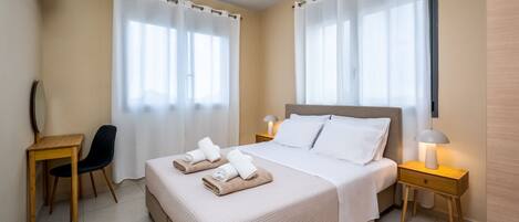 A hotel room with a bed, two bedside tables, a desk, a chair, and a window with curtains.