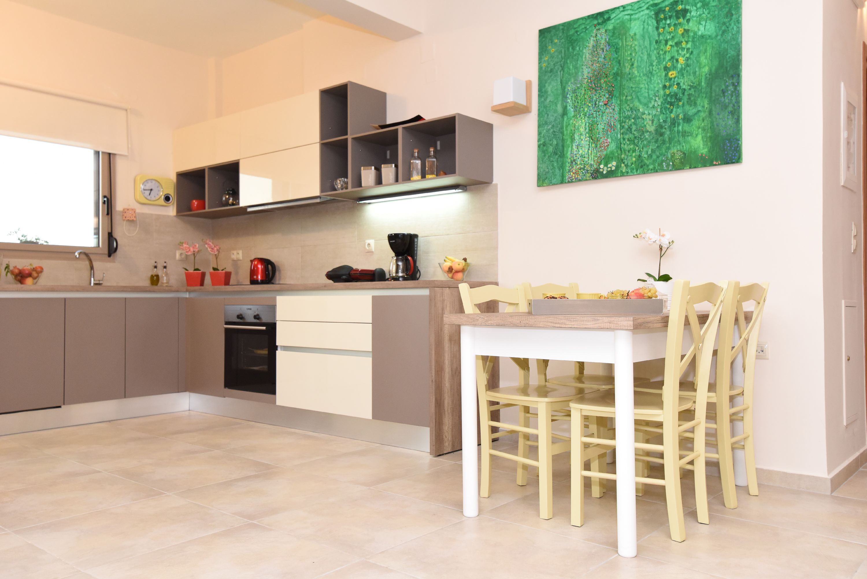A modern kitchen with built-in appliances, a dining area with a table and chairs, and a green abstract painting on the wall.