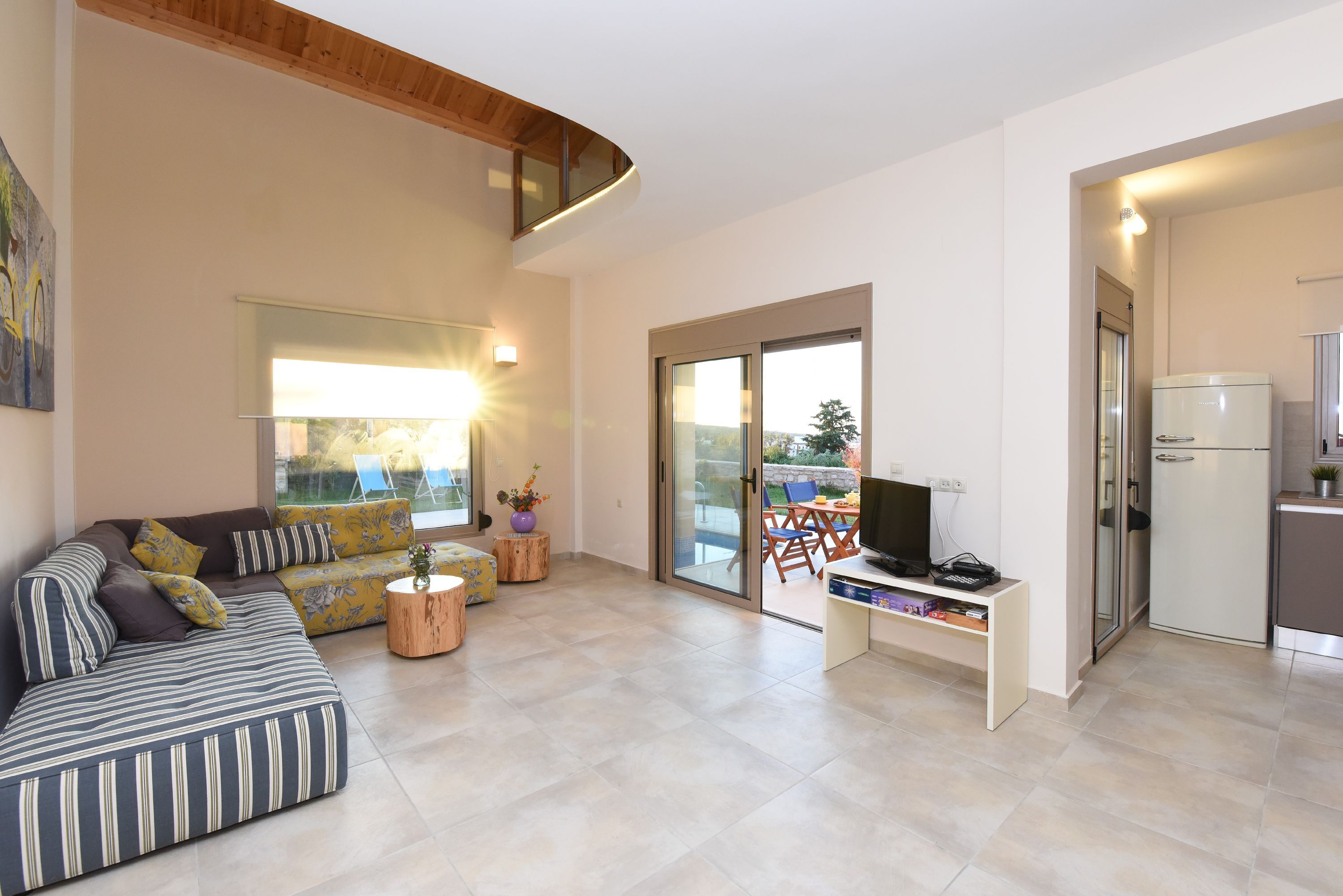A modern living room with a sofa, a coffee table, a TV, and a kitchen area with a refrigerator.