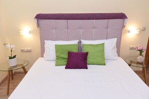 A bed with a striped headboard, two pillows, a glass table with a vase, and a wall socket. - Mon Emvasia Margarites Villa B (Mylopotamos)