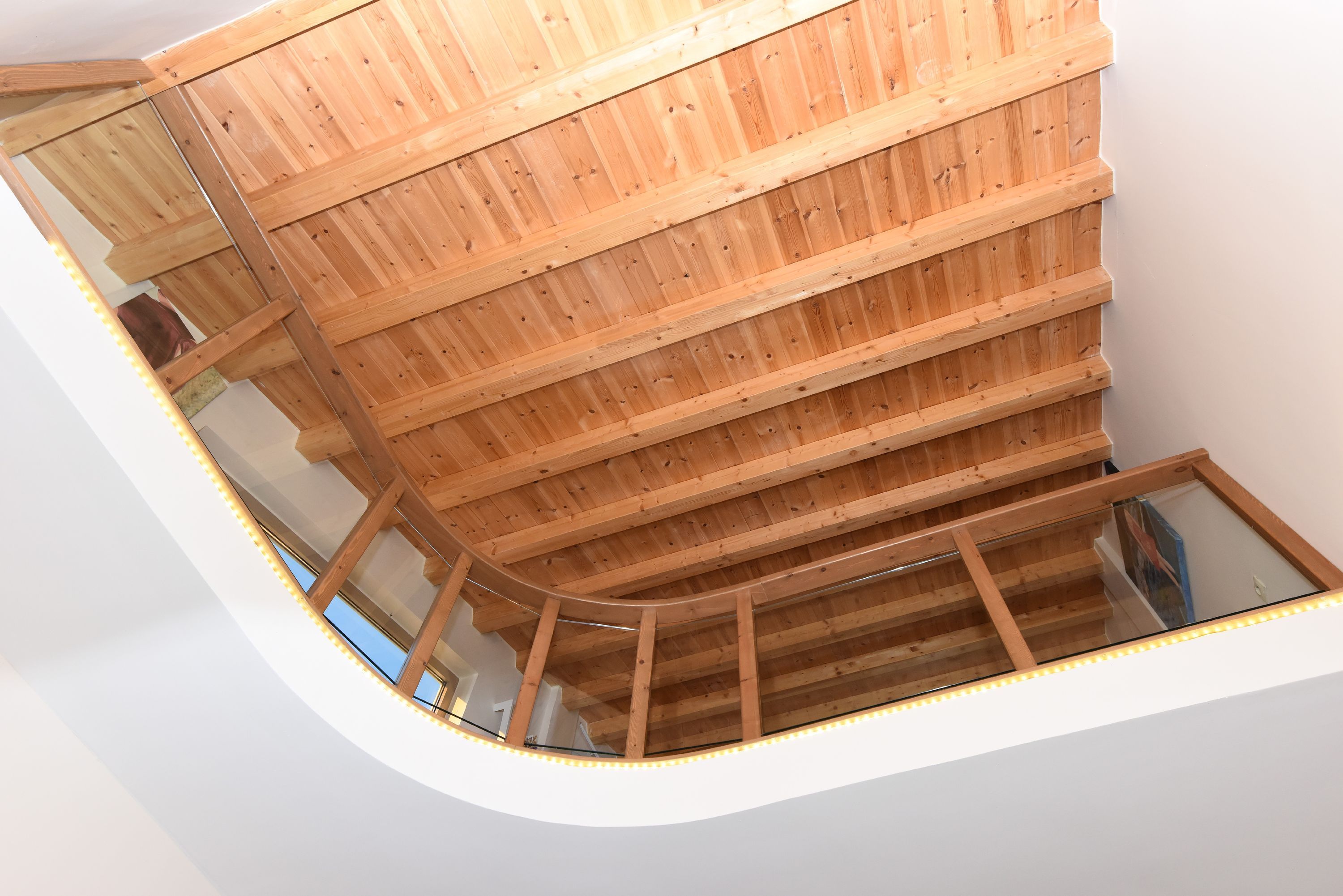 Een hoge plafond met houten balken en een glazen balkonhek.