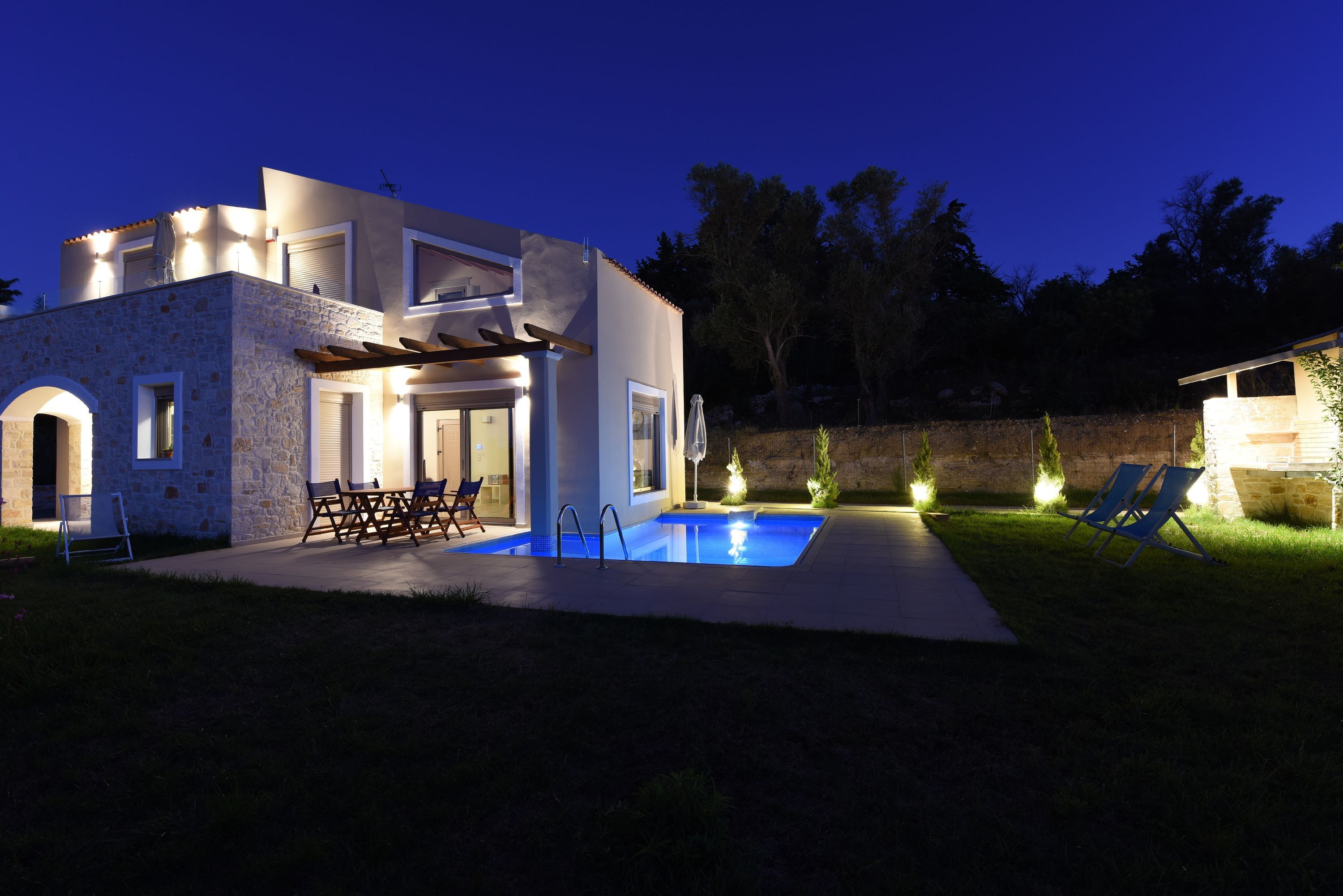 A modern house with a swimming pool, outdoor seating, and a stone facade.