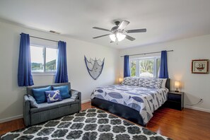 Un dormitorio con cama, sofá gris, ventilador de techo y ventana con cortinas.