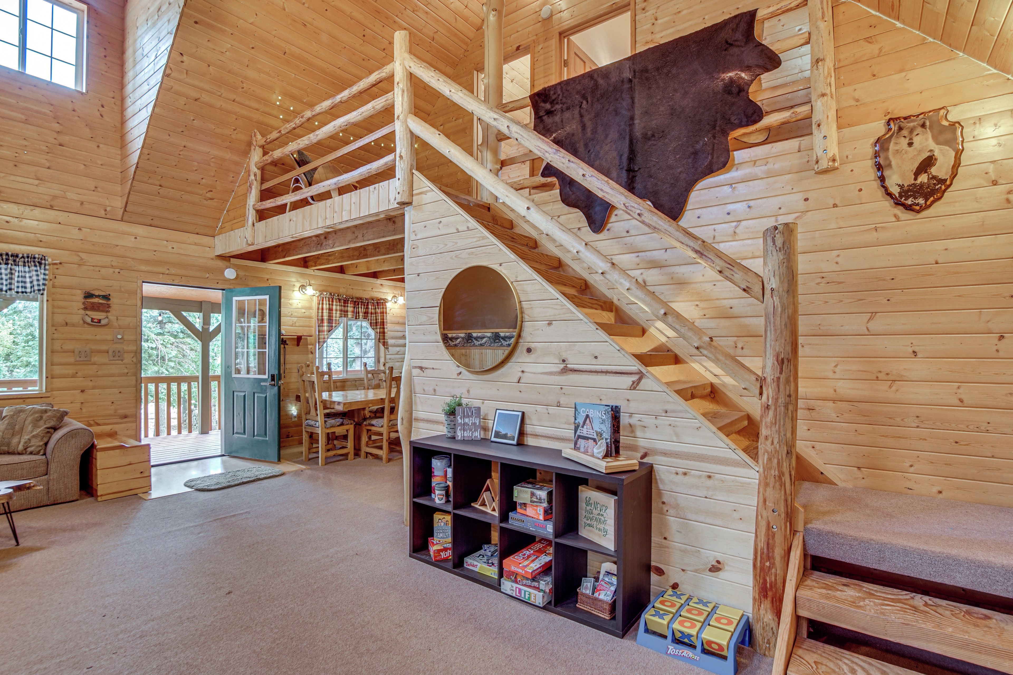 A wooden cabin interior with a staircase, a mounted animal hide, and a bookshelf with various items.