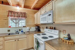 Una cocina con armarios de madera, un microondas, una estufa y una ventana con cortina a cuadros.