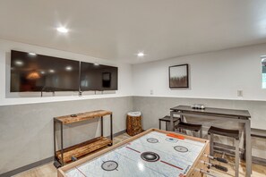 A room with a foosball table, a TV mounted on the wall, and a small table with chairs. - Game Room, Fire Pit: Dog-Friendly Duck Creek Cabin (Duck Creek Village)