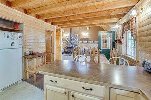 A wooden interior with a kitchen area featuring a refrigerator, a dining table with chairs, and a stone wall with a fireplace. - Game Room, Fire Pit: Dog-Friendly Duck Creek Cabin (Duck Creek Village)