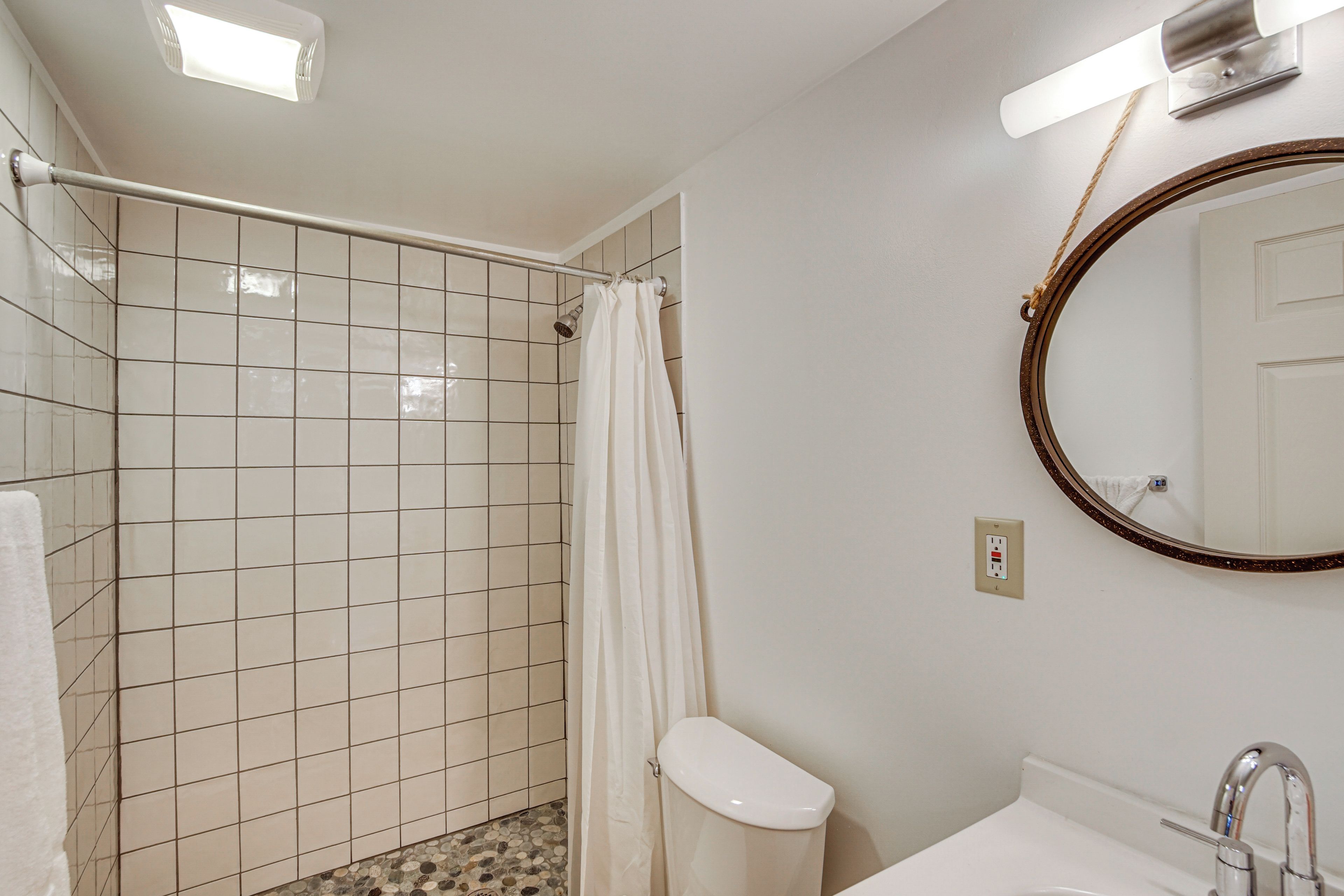 A bathroom with a shower, toilet, sink, and a mirror.