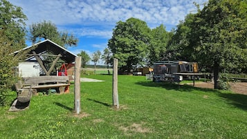 Eine ländliche Außenansicht mit einer Holzhütte, einem überdachten Bereich und einem Fahrzeug.