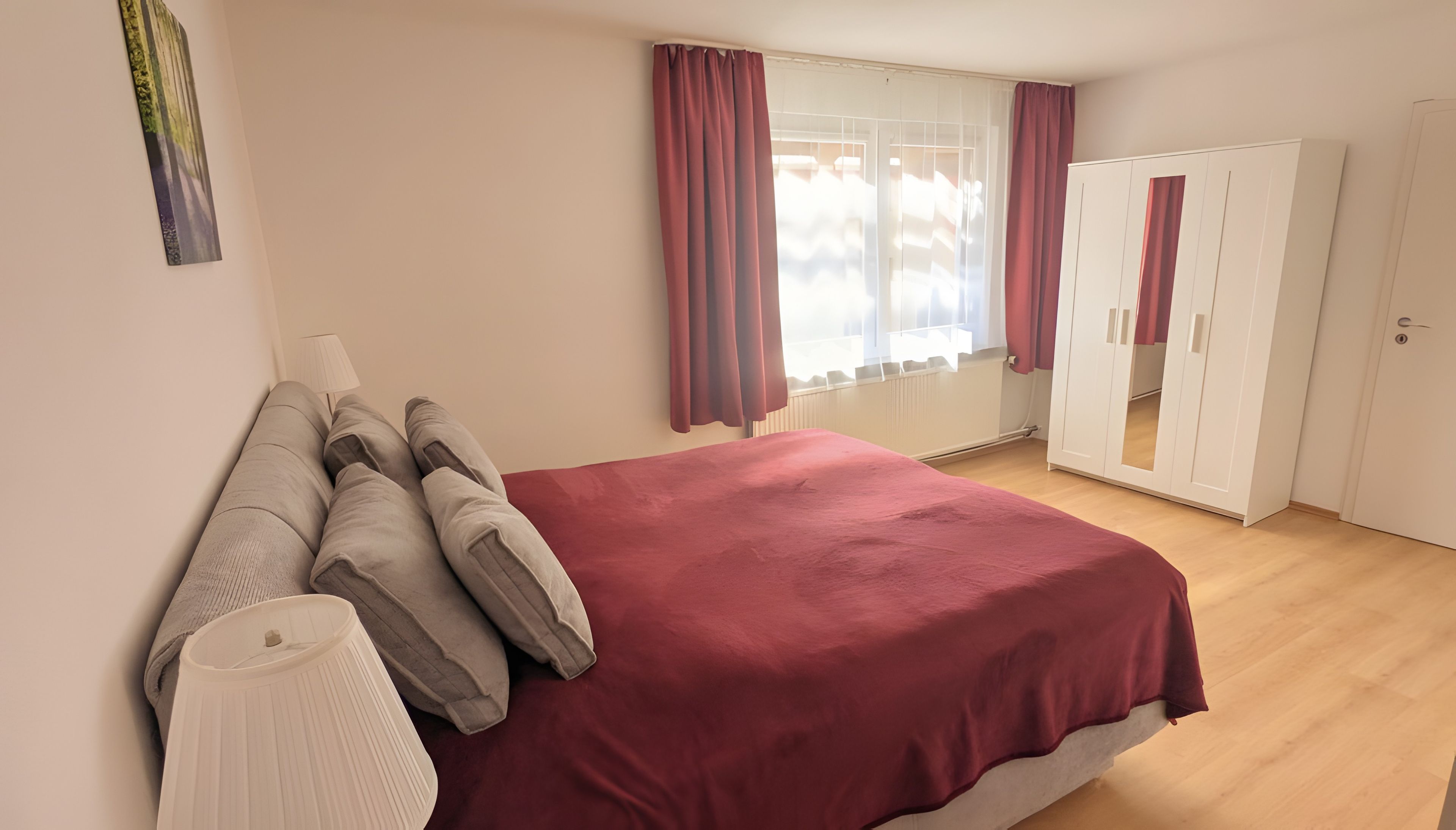 A bedroom with a bed, a wardrobe, a window with curtains, and a wall-mounted lamp.