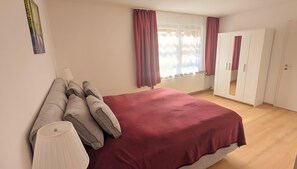 A bedroom with a bed, a wardrobe, a window with curtains, and a wall-mounted lamp.