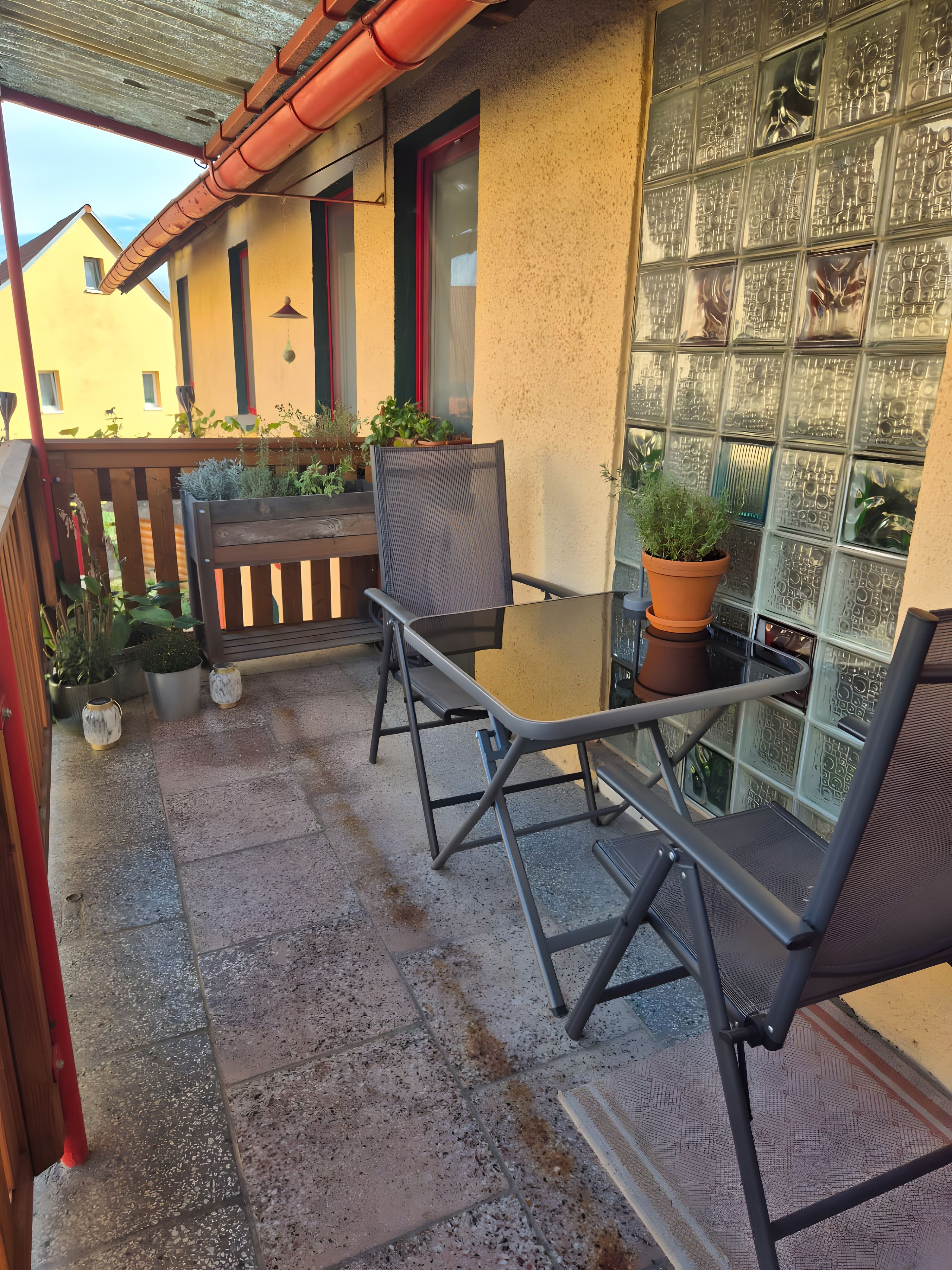 An outdoor patio with a table and chairs, potted plants, and a view of a building with patterned windows.