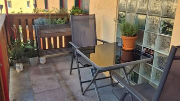 An outdoor patio with a table and chairs, potted plants, and a view of a building with patterned windows.