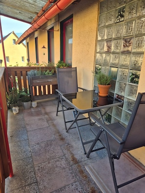An outdoor patio with a table and chairs, potted plants, and a view of a building with patterned windows.