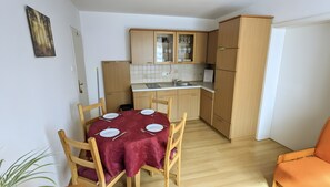 A compact kitchen with wooden cabinets, a dining table with chairs, and a small orange chair.