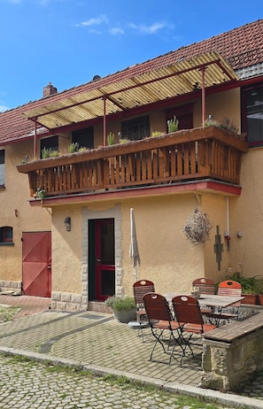 Ein Gebäude mit roter Tür, einem Balkon mit Holellentrailierungen und Außenbestuhlung.