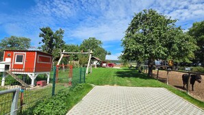 Ett inhägnat utomhusområde med en röd byggnad, en träkonstruktion och ett svart djur.